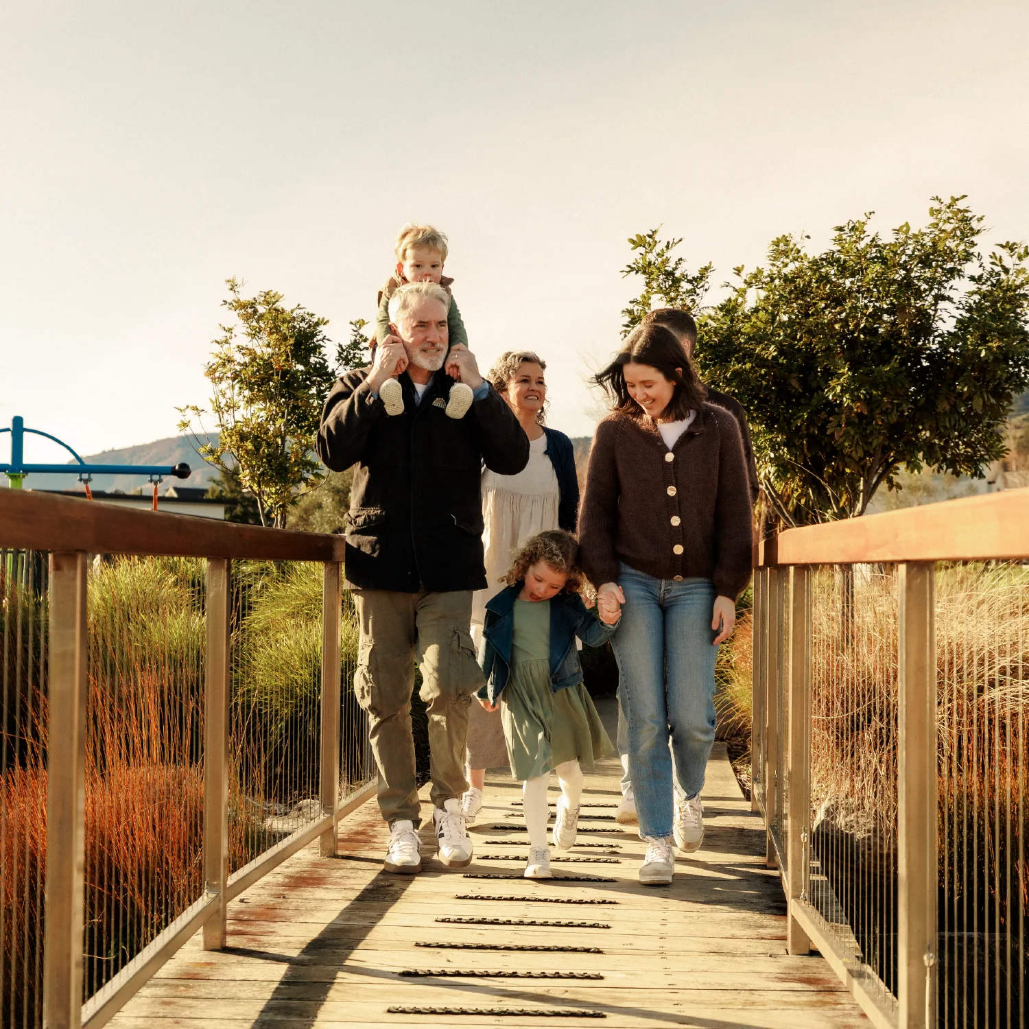 Multi-generational family walking across a wooden bridge together at Olive Estate Lifestyle Village.