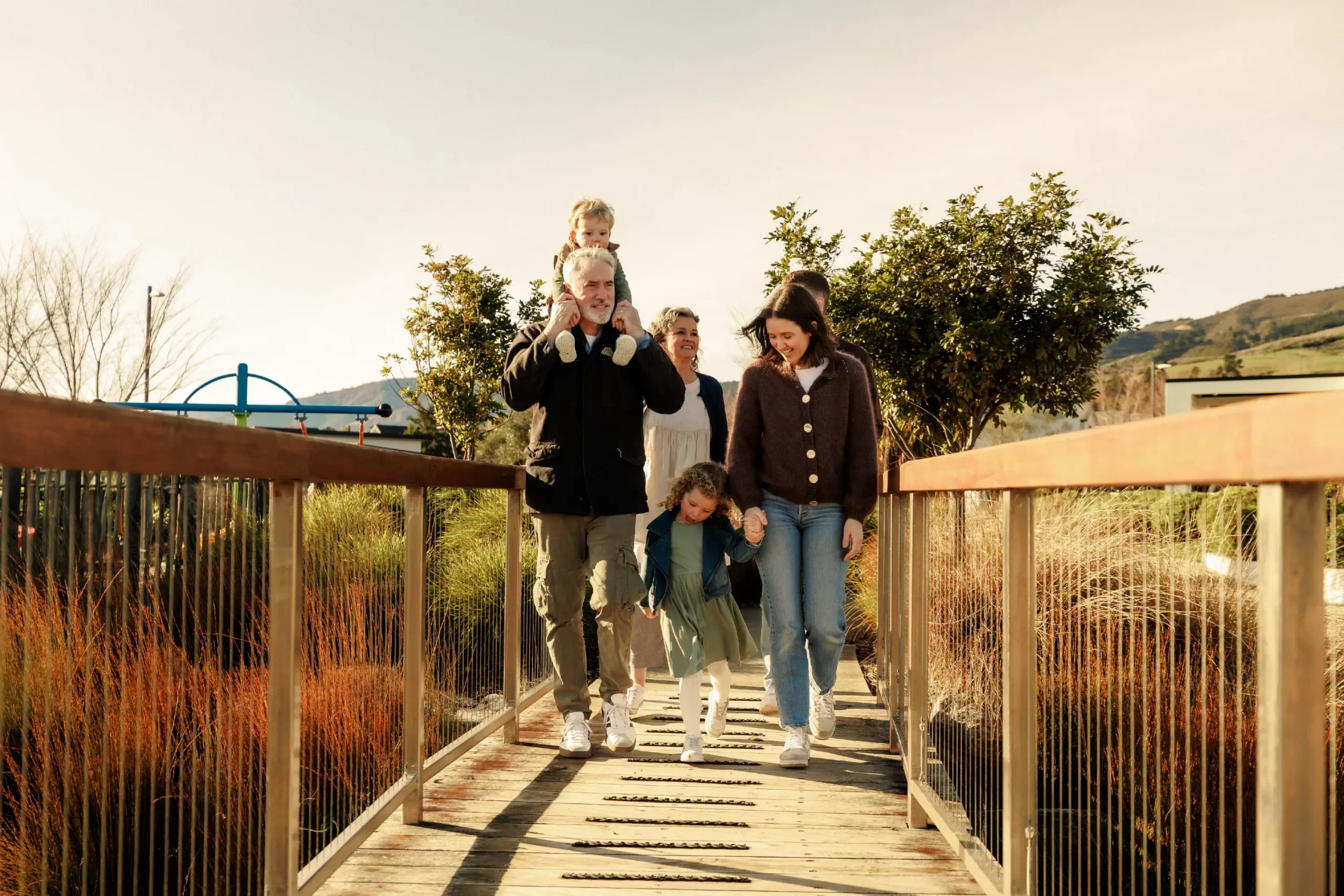 Multi-generational family walking across a wooden bridge together at Olive Estate Lifestyle Village.