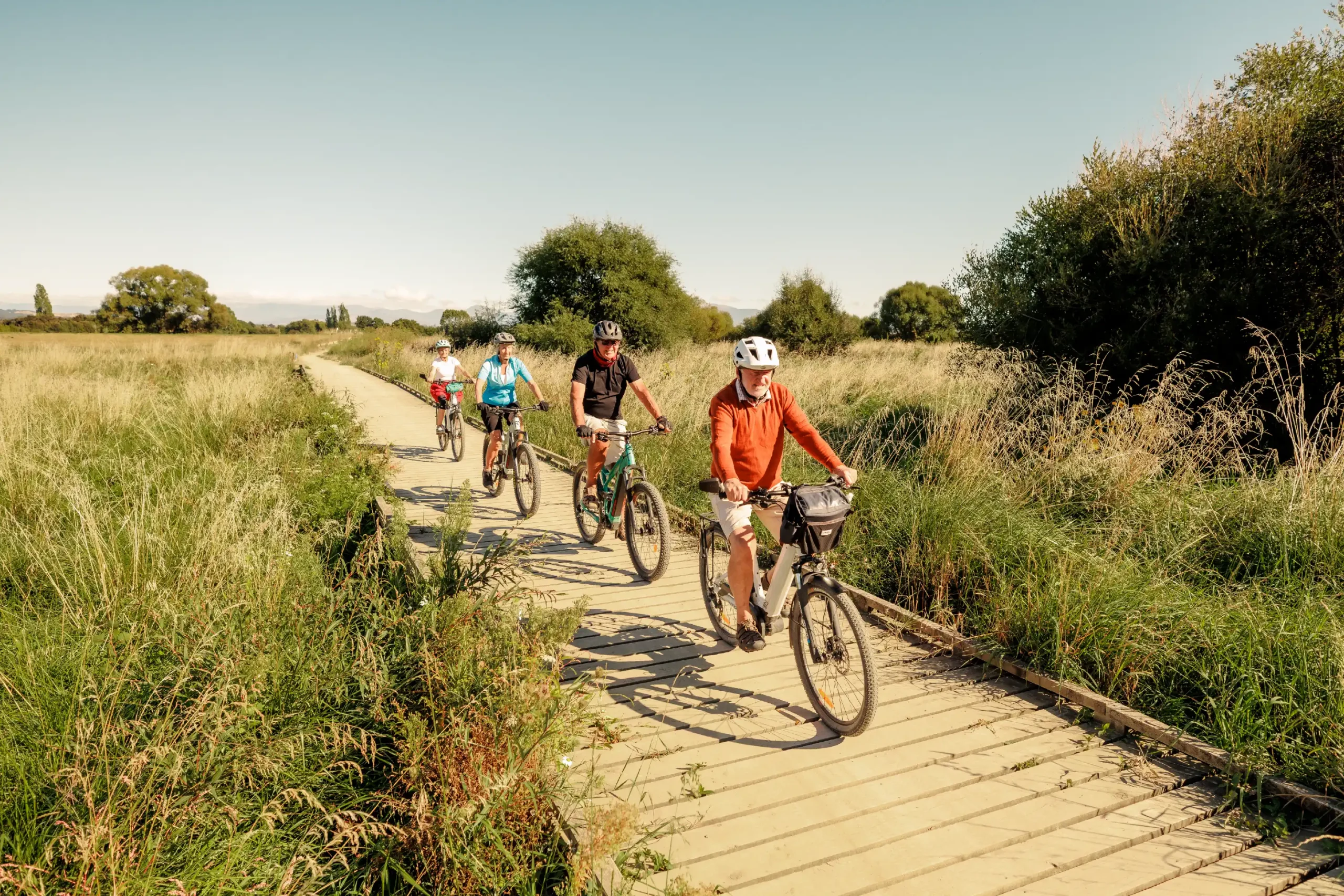 Group of cyclists riding along a wooden boardwalk on the Great Taste Trail near Olive Estate Lifestyle Village.